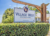 Thumbnail 28 of 46 - A sign for Village West Apartment Homes stands in front of a building.
