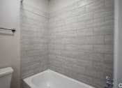 Thumbnail 60 of 62 - A white bathtub sits in a bathroom with a grey tiled wall.