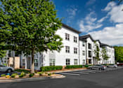 Thumbnail 5 of 57 - A white building with a parking lot in front.