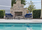 Thumbnail 15 of 35 - A pool with a stone fireplace and two chairs.