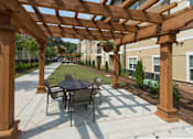 Thumbnail 15 of 91 - A wooden pergola with a table and chairs is in the foreground of a patio area.