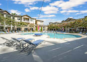 Thumbnail 10 of 91 - A pool area with sun loungers and a building in the background.