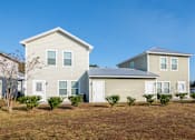 Thumbnail 12 of 47 - A house with a grey roof and white trim is surrounded by bushes and has a clear blue sky in the background.