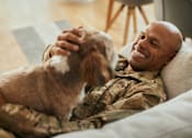 Thumbnail 9 of 11 - A man in military uniform is laughing while holding a dog.