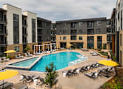 Thumbnail 57 of 81 - A large swimming pool surrounded by lounge chairs and umbrellas in front of apartment buildings.