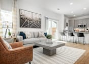 Thumbnail 20 of 52 - A modern living room with a brown armchair, a grey sofa, a coffee table, and a kitchen area in the background.