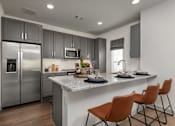 Thumbnail 1 of 52 - A modern kitchen with a refrigerator, microwave, and a counter with chairs.