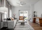 Thumbnail 2 of 52 - A living room with a grey couch, a grey rug, a white coffee table, a wooden bench, a floor lamp, a ceiling fan, and a window with blinds.