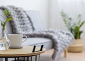 Thumbnail 10 of 11 - A clear glass vase with a plant sits on a table next to a white mug.