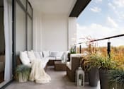 Thumbnail 7 of 11 - A modern outdoor living space with a couch, pillows, and plants.
