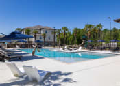 Thumbnail 3 of 12 - resort style swimming pool surrounded by lounge chairs and umbrellas at Beau Chene Lake Charles Apartments in Lake Charles, LA 70605