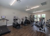 Thumbnail 9 of 12 - a gym with cardio machines and other exercise equipment on a wooden floor at Beau Chene Lake Charles Apartments in Lake Charles, LA 70605