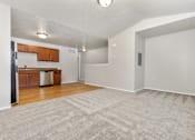 Thumbnail 21 of 60 - A spacious room with a carpeted floor and a kitchen area with wooden cabinets and a stainless steel dishwasher.