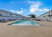 Thumbnail 8 of 60 - A swimming pool in a sunny day surrounded by chairs and buildings.