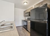 Thumbnail 7 of 21 - A black refrigerator is in the corner of a kitchen with a sink and microwave above it.