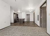 Thumbnail 36 of 59 - A spacious room with a carpeted floor and a kitchen area in the background.