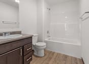 Thumbnail 27 of 44 - A white toilet sits in a bathroom with a wooden floor and a white tub.