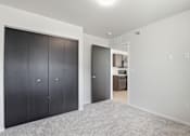 Thumbnail 34 of 68 - A room with a white wall and a carpeted floor with a black door on the left and a white door on the right.