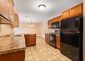 Thumbnail 18 of 64 - A kitchen with a black refrigerator, brown cabinets, and a granite countertop.