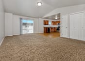Thumbnail 53 of 60 - A spacious living room with a carpeted floor and a kitchen area in the background.
