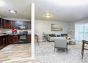 Thumbnail 1 of 41 - A living room with a grey couch and a kitchen area with brown cabinets.