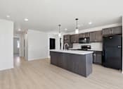 Thumbnail 43 of 68 - A kitchen with a black fridge and microwave, brown cabinets, and a white countertop.