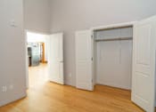Thumbnail 2 of 9 - A room with white walls and wooden floors, with a doorway leading to another room.