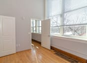 Thumbnail 7 of 9 - A room with white walls and wooden floors has two white doors and a window with blinds.