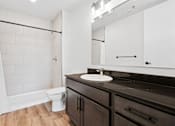 Thumbnail 48 of 73 - A bathroom with a white shower curtain, a white toilet, a sink with a mirror above it, and a black counter.