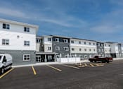 Thumbnail 1 of 16 - A parking lot with a white van and a red truck parked in front of a building.