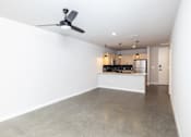 Thumbnail 15 of 41 - A room with a ceiling fan and a kitchen area in the background.