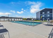 Thumbnail 51 of 58 - A pool area with sun loungers and a building in the background.