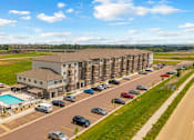 Thumbnail 1 of 38 - A large apartment complex with a pool and cars parked in the parking lot.