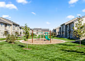 Thumbnail 27 of 37 - A playground with a green slide in the middle of a grassy area surrounded by houses.