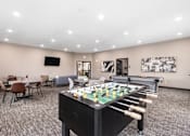 Thumbnail 9 of 31 - A foosball table is in the middle of a room with chairs and a TV.