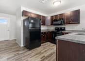 Thumbnail 4 of 26 - A black refrigerator stands in a kitchen with wooden cabinets and a marble countertop.