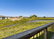 Thumbnail 24 of 26 - A wooden deck overlooks a grassy field with a river and houses in the distance.