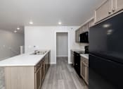 Thumbnail 7 of 26 - A modern kitchen with a black refrigerator and wooden cabinets.