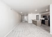 Thumbnail 6 of 26 - A spacious room with a carpeted floor and a kitchen area in the background.