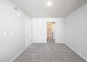 Thumbnail 21 of 26 - A white room with a carpeted floor and a doorway leading to another room.