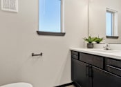 Thumbnail 24 of 43 - A bathroom with a white toilet, a sink with a plant on it, and a window.