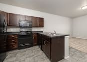 Thumbnail 16 of 26 - A kitchen with brown cabinets and a black refrigerator.