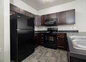 Thumbnail 25 of 26 - A kitchen with black appliances and brown cabinets.