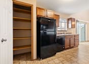 Thumbnail 59 of 64 - A black refrigerator is in a kitchen with wooden cabinets and a white door.
