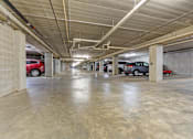 Thumbnail 7 of 54 - A parking garage with concrete floors and walls, and cars parked in the background.