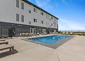 Thumbnail 22 of 44 - A large outdoor swimming pool is surrounded by a concrete patio and wooden benches.