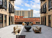 Thumbnail 13 of 42 - A patio with chairs and a table is surrounded by buildings.