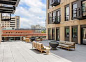 Thumbnail 14 of 42 - A patio with wooden furniture and a fire pit.