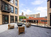 Thumbnail 15 of 42 - A patio with a table and chairs is surrounded by buildings.