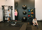 Thumbnail 7 of 42 - A woman is sitting on a mat in a gym, stretching her legs.